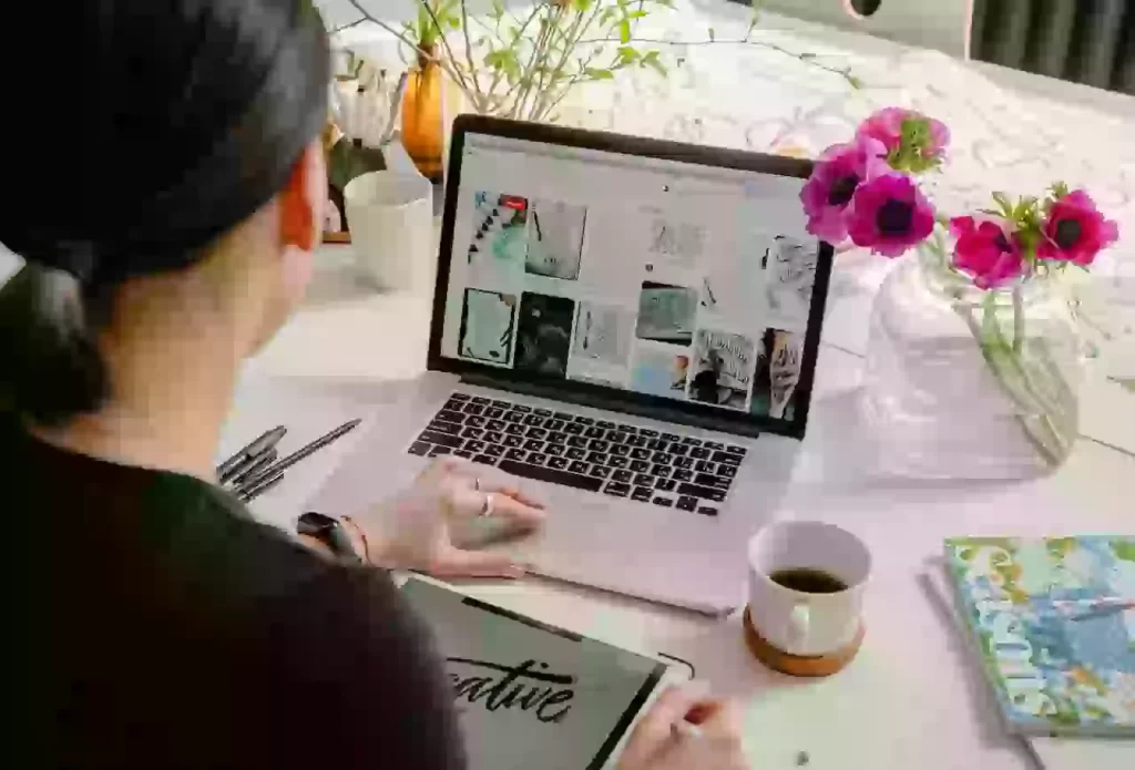 Woman working on laptop with coffee and flowers.